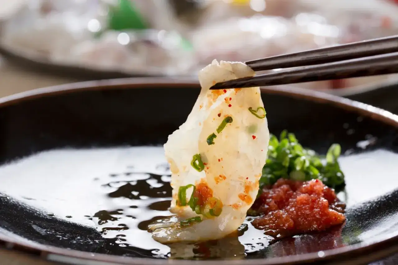Wykwintne fugu sushi, delikatny płatek ryby z zieloną cebulką i pikantnym ikrą, podniesiony pałeczkami.
