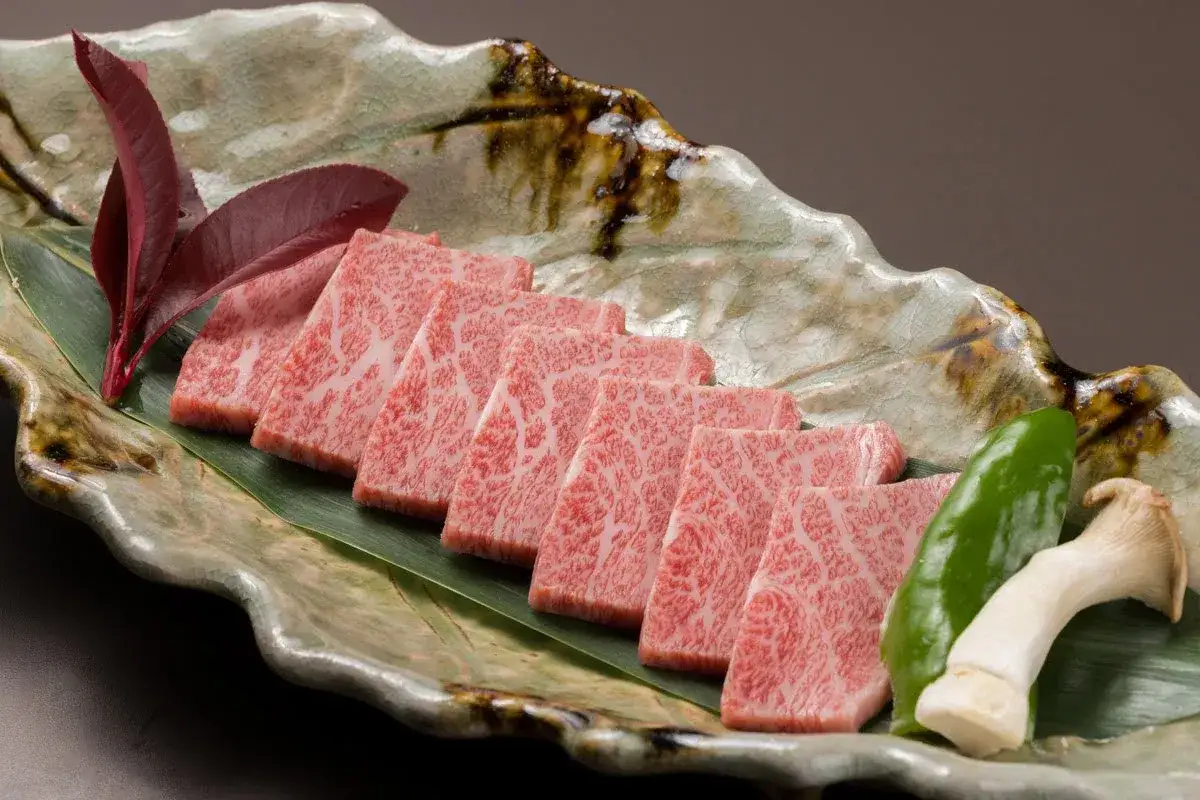 Kawałki soczystych krowy wagyu ułożone na liściu, ozdobione papryczką i grzybem.