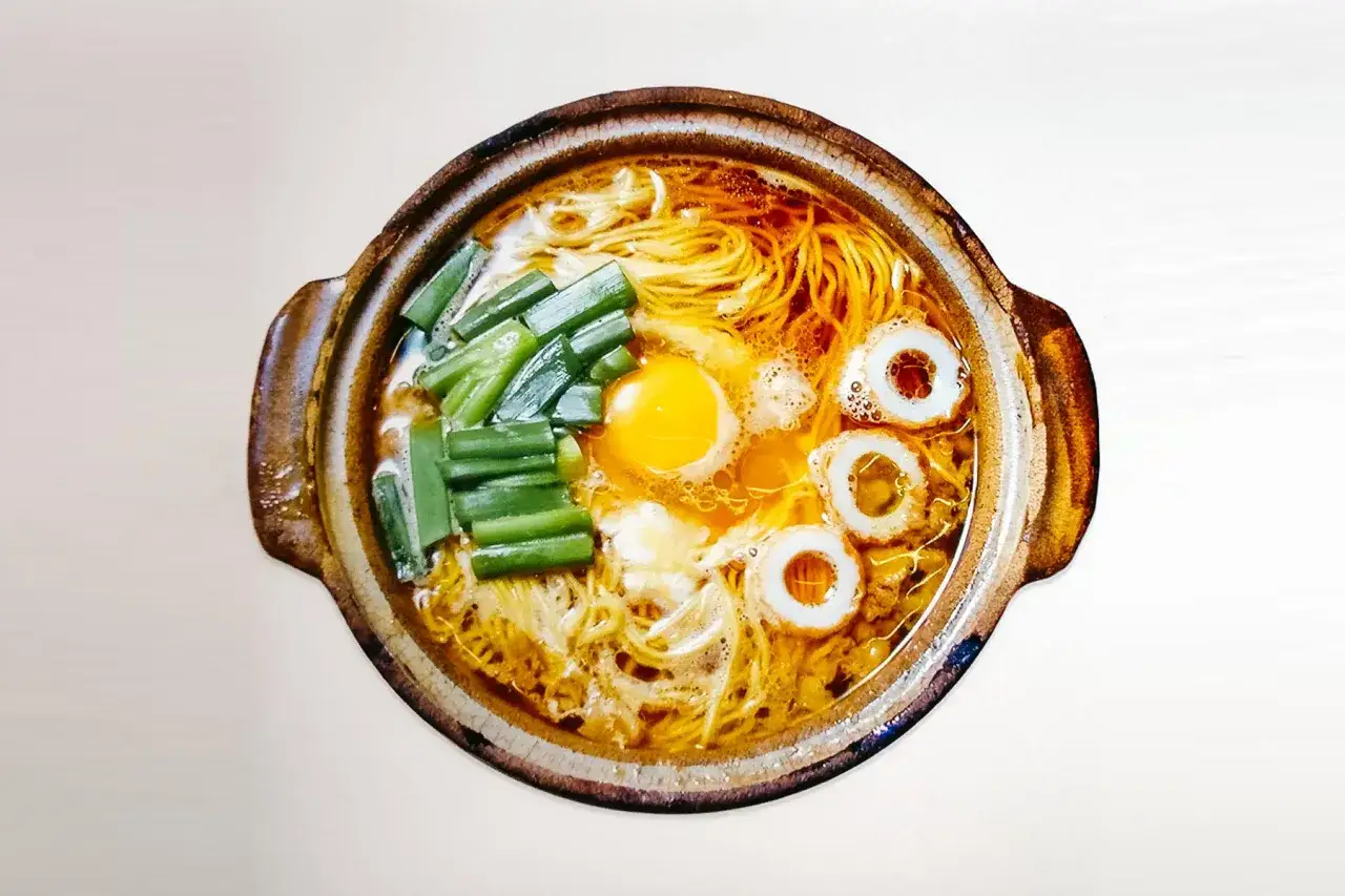 Gorący udon ramen z jajkiem sadzonym, szczypiorkiem i rybnymi krążkami w glinianej misce.