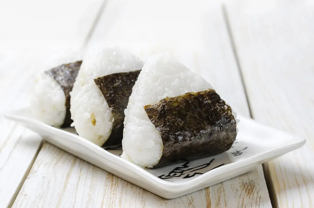 Trzy pyszne onigiri z kurczakiem, owinięte w chrupiące wodorosty nori, ułożone na białym talerzyku.