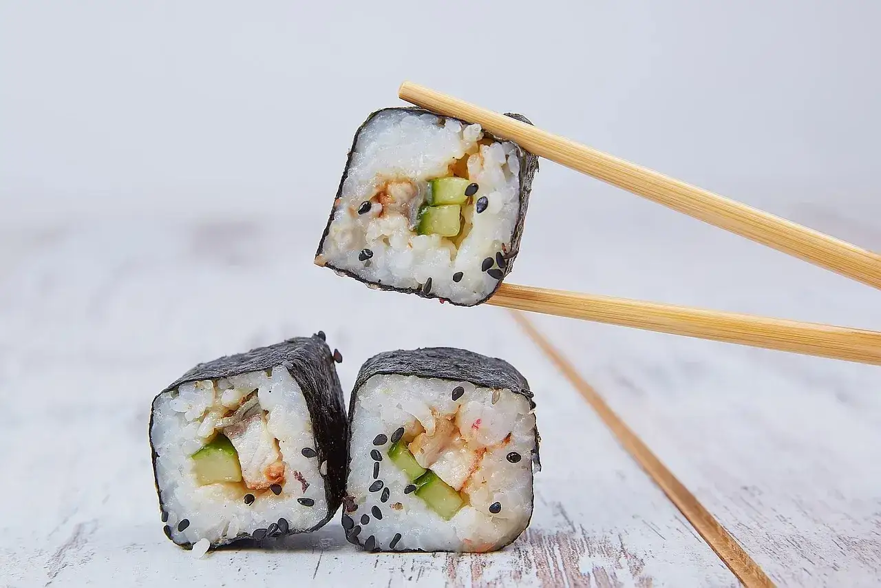 Rolka sushi z ogórkiem i rybą, podniesiona pałeczkami. Zastanawiasz się, ile octu do sushi?