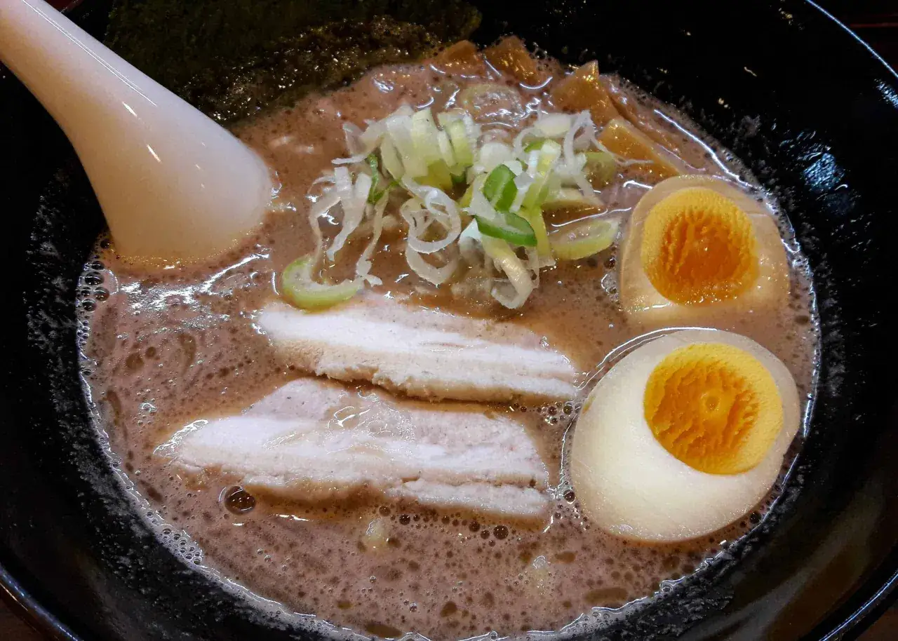 Aksamitny bulion, plastry boczku, jajko na p&oacute;ł i szczypiorek w misce z ramen.