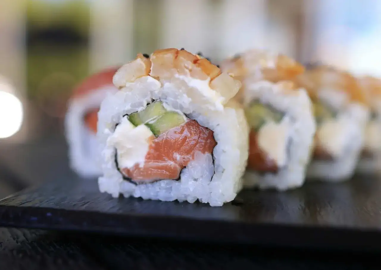 Uramaki co to? Rolka sushi z łososiem, awokado i krewetkami, ryż na zewnątrz, podana na czarnej desce.