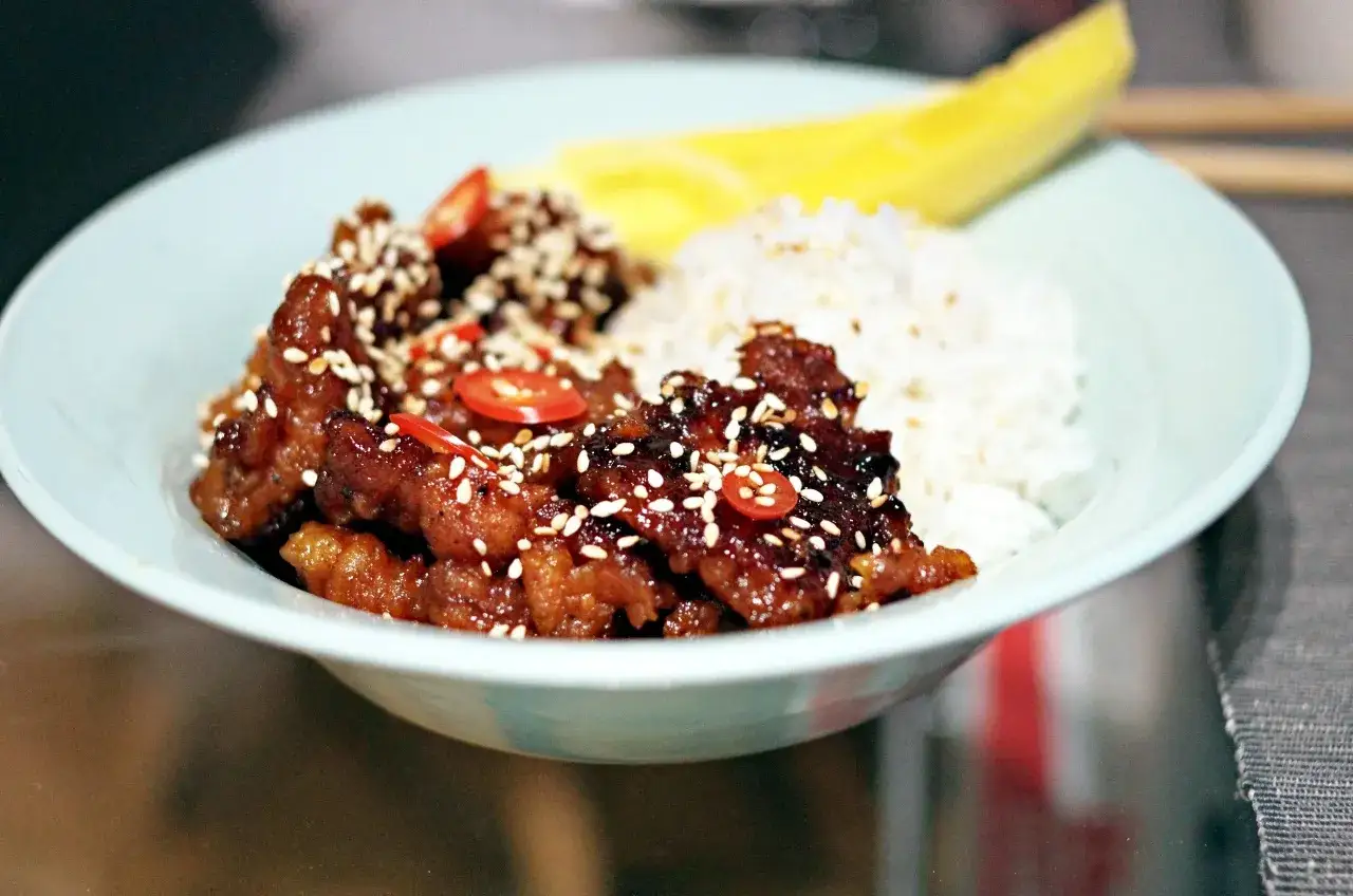 Pyszny boczek po koreańsku w sosie, posypany sezamem i chili, podany z ryżem i kawałkiem mango.
