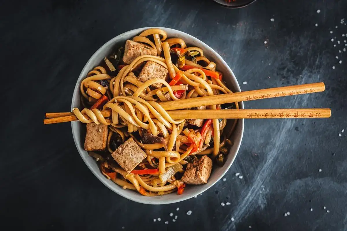 Miseczka pełna makaronu udon z tofu i warzywami, gotowa do jedzenia.