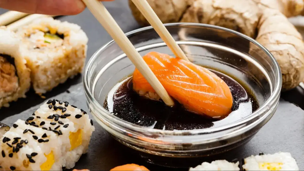 Kawałek łososia zanurzany w sosie sojowym, obok sushi i imbiru. Idealne sosy do sushi podkreślają smak.