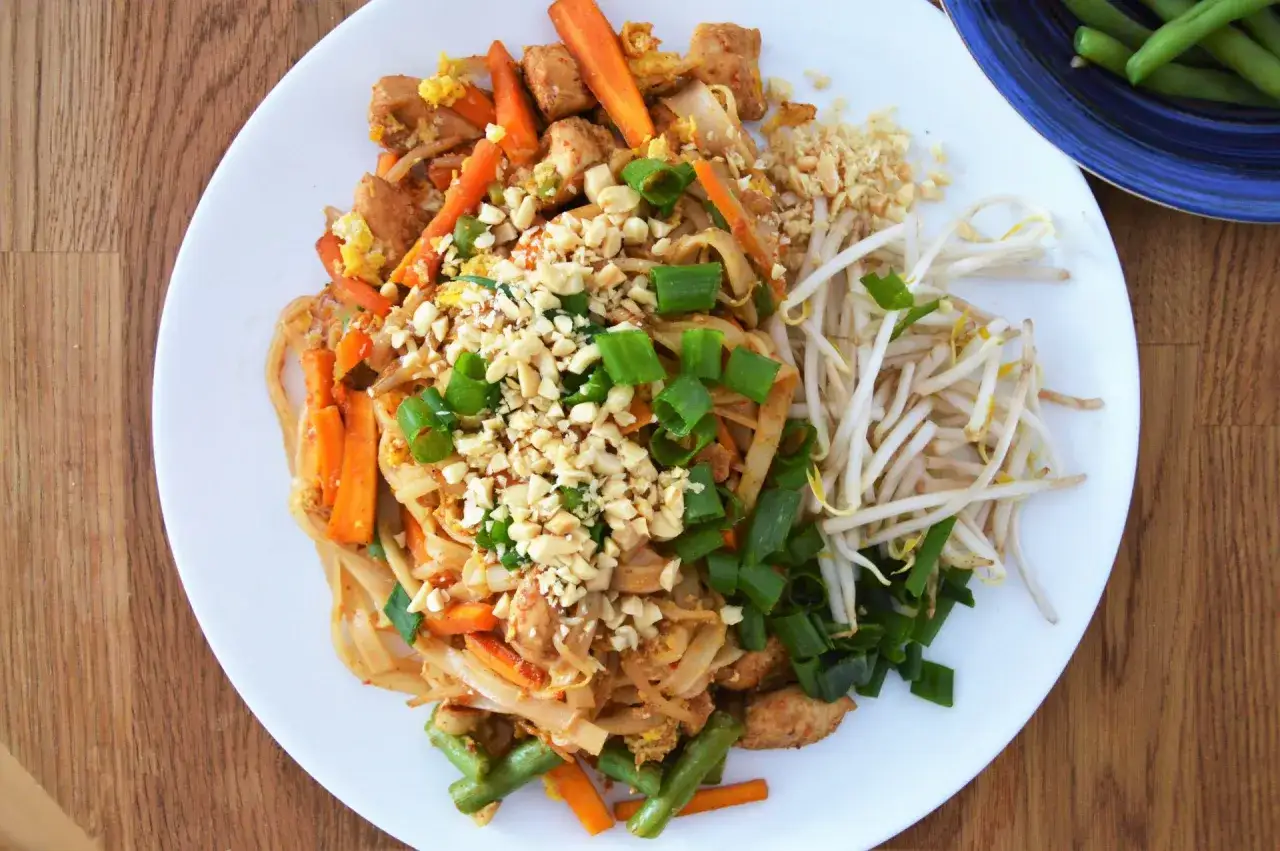 Pyszny pad thai z jajkiem, kurczakiem, marchewką i orzeszkami ziemnymi, podany z kiełkami fasoli mung.