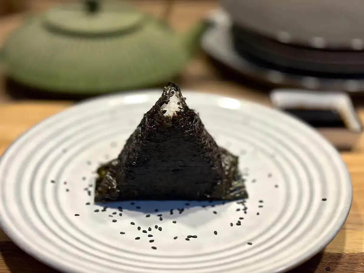 Trójkątne onigiri z tuńczykiem, owinięte w nori, na talerzu z sezamem.