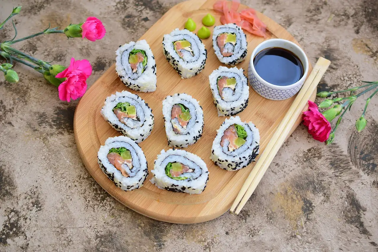 Pyszne rolki california roll z łososiem i awokado, posypane sezamem, podane z sosem sojowym i imbirem.