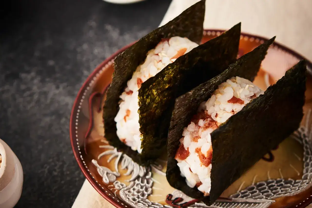 Trzy onigiri zawinięte w nori, czyli jadalne wodorosty. Ryż z kawałkami łososia i sezamem.