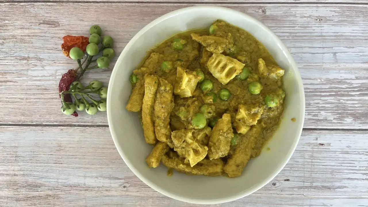Aromatic jungle curry z kawałkami ryby i zielonym groszkiem, podane z gałązką zielonych pomidorków i suszonymi papryczkami.