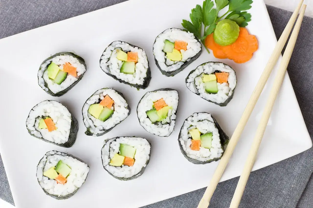 Talerz z futomaki i uramaki, czyli rolkami sushi z awokado, og&oacute;rkiem i marchewką. Obok pałeczki i dekoracja z wasabi.