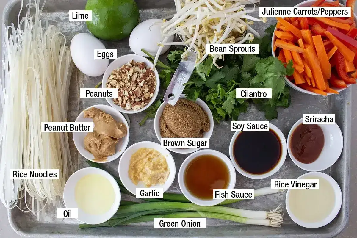 Składniki do sosu pad thai: makaron ryżowy, jajka, orzeszki ziemne, masło orzechowe, limonka, kiełki fasoli, kolendra, marchewka, papryka, brązowy cukier, sos sojowy, sos rybny, czosnek, olej, zielona cebulka, sriracha, ocet ryżowy.