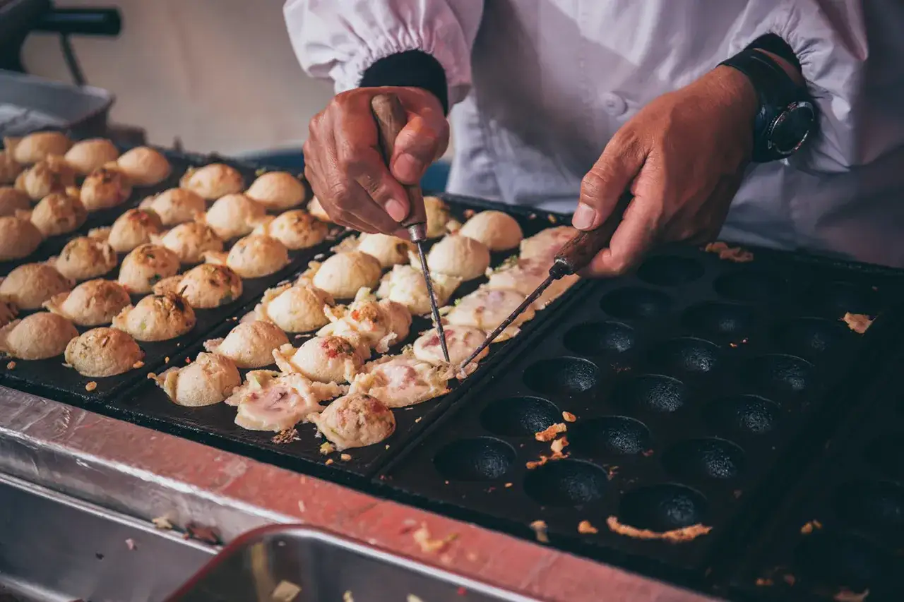 Ręce obracają kulki takoyaki na specjalnej patelni. To idealny takoyaki przepis, który pozwala stworzyć te japońskie przysmaki.