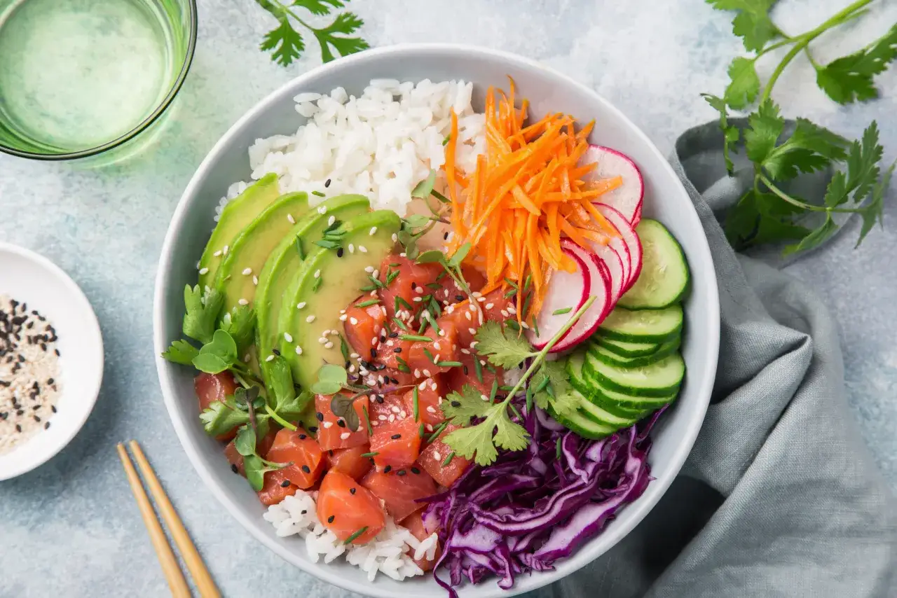 Kolorowa bowl sushi z łososiem, awokado, ryżem, marchewką, rzodkiewką i ogórkiem.