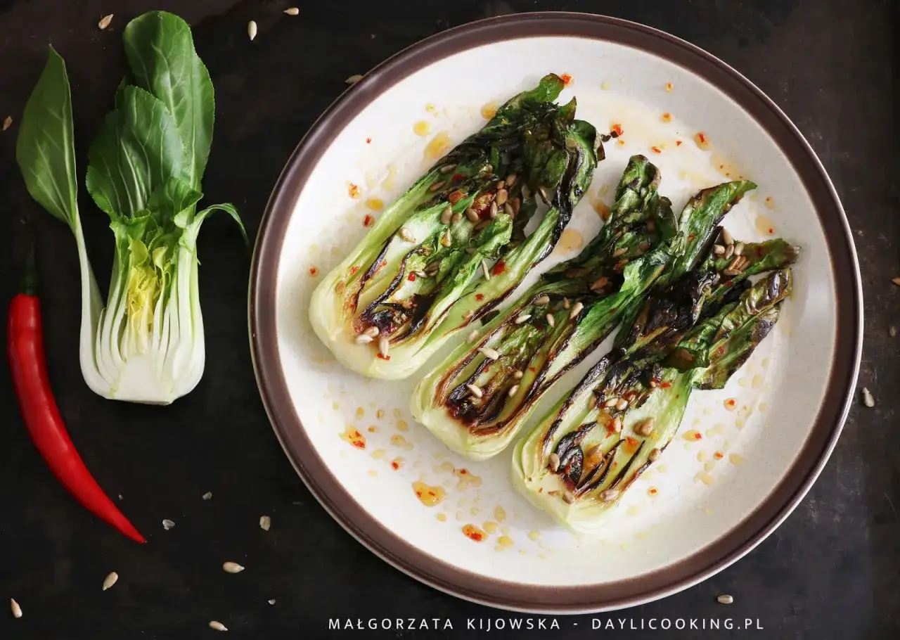 Grillowana sałata pak choi z nasionami słonecznika i chili, obok czerwona papryczka.