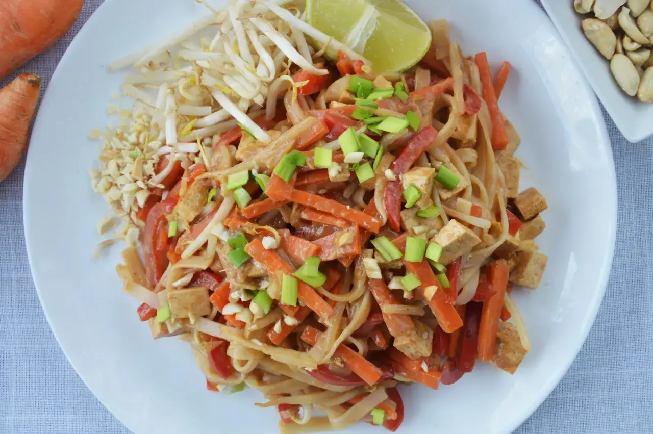 Pyszne pad thai z warzywami, chrupiącą marchewką, papryką i tofu, posypane szczypiorkiem i orzeszkami.