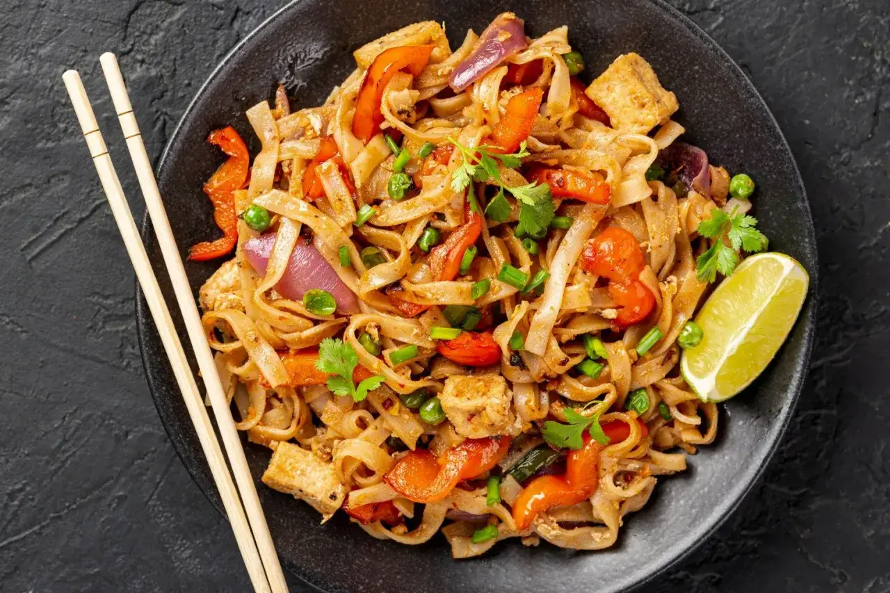 Pyszne pad thai z jajkiem, warzywami i tofu, podane z limonką i pałeczkami.