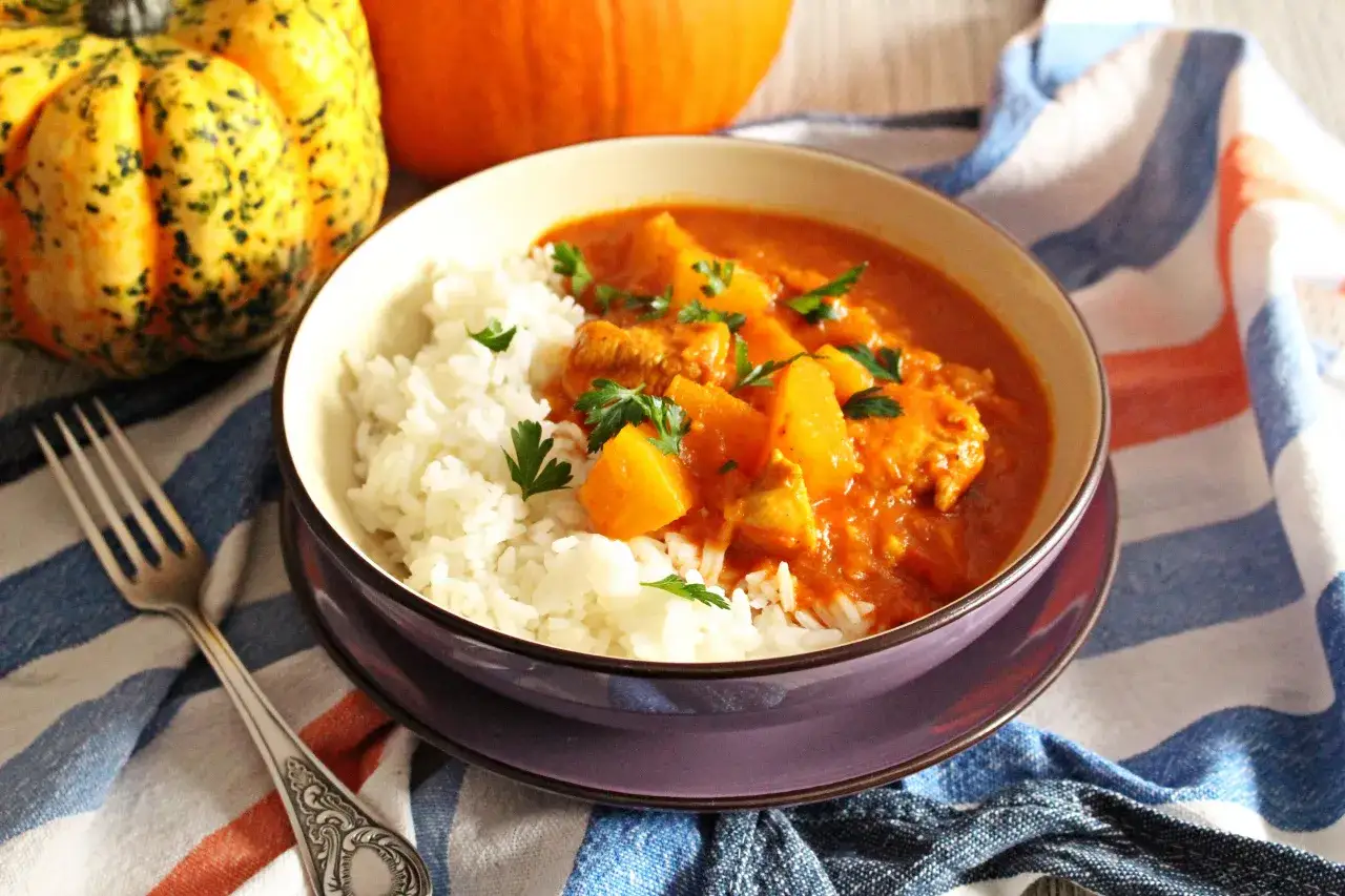 Aksamitny kurczak curry z dynią i mlekiem kokosowym, podany z ryżem. Obok dynie i widelczyk.