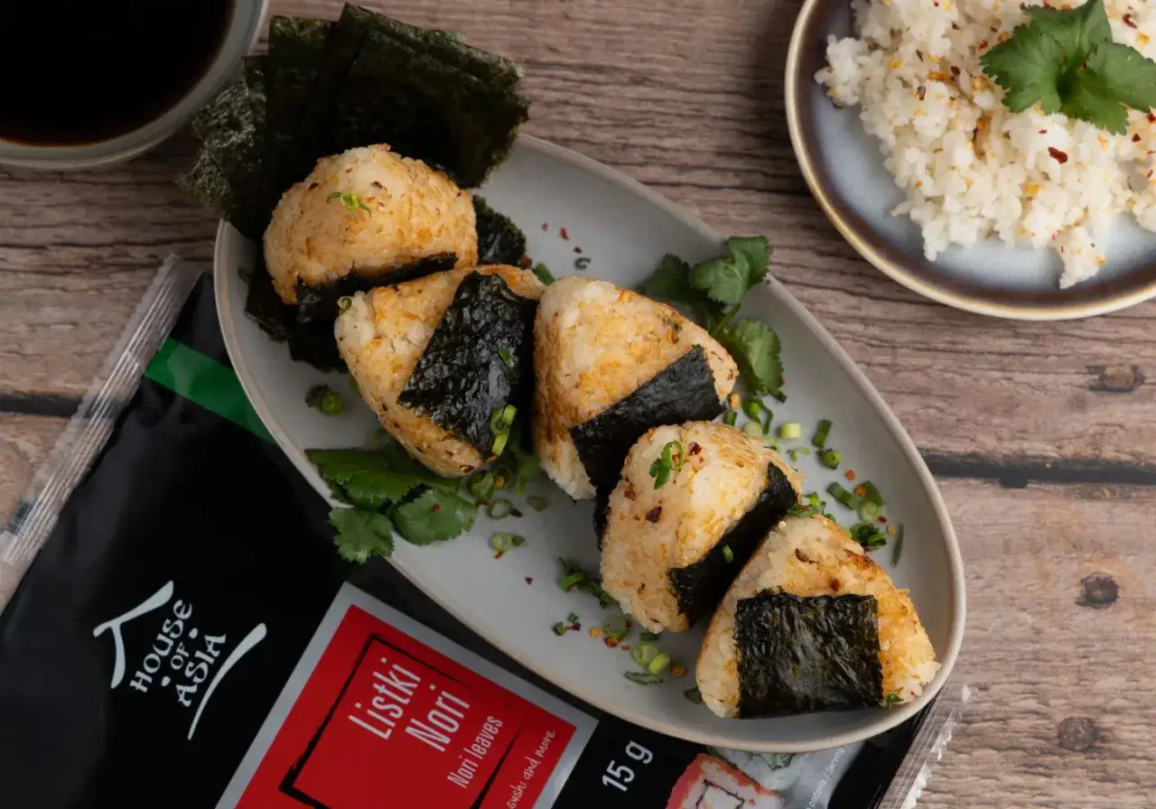 Pięć pysznych onigiri z ryżu, owiniętych w nori, gotowych do spożycia. Obok opakowanie listk&oacute;w nori.