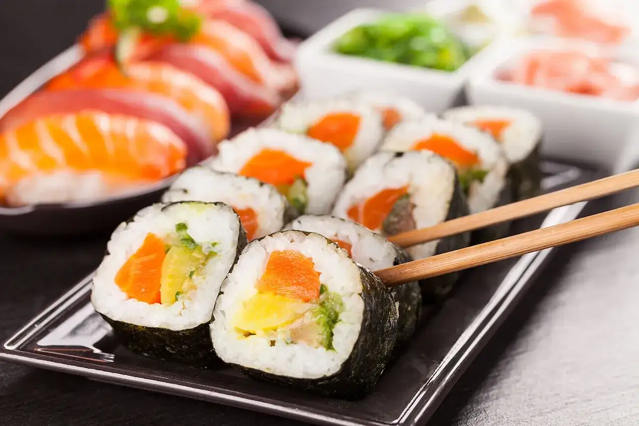 Uramaki co to? Rolka sushi z ryżem na zewnątrz, z łososiem i warzywami, podana z pałeczkami.
