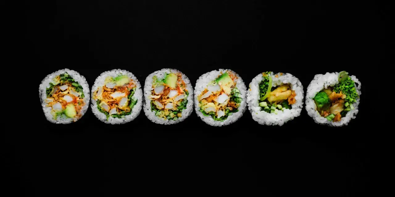 Sześć kawałk&oacute;w sushi: futomaki i uramaki z awokado, kurczakiem i warzywami na czarnym tle.