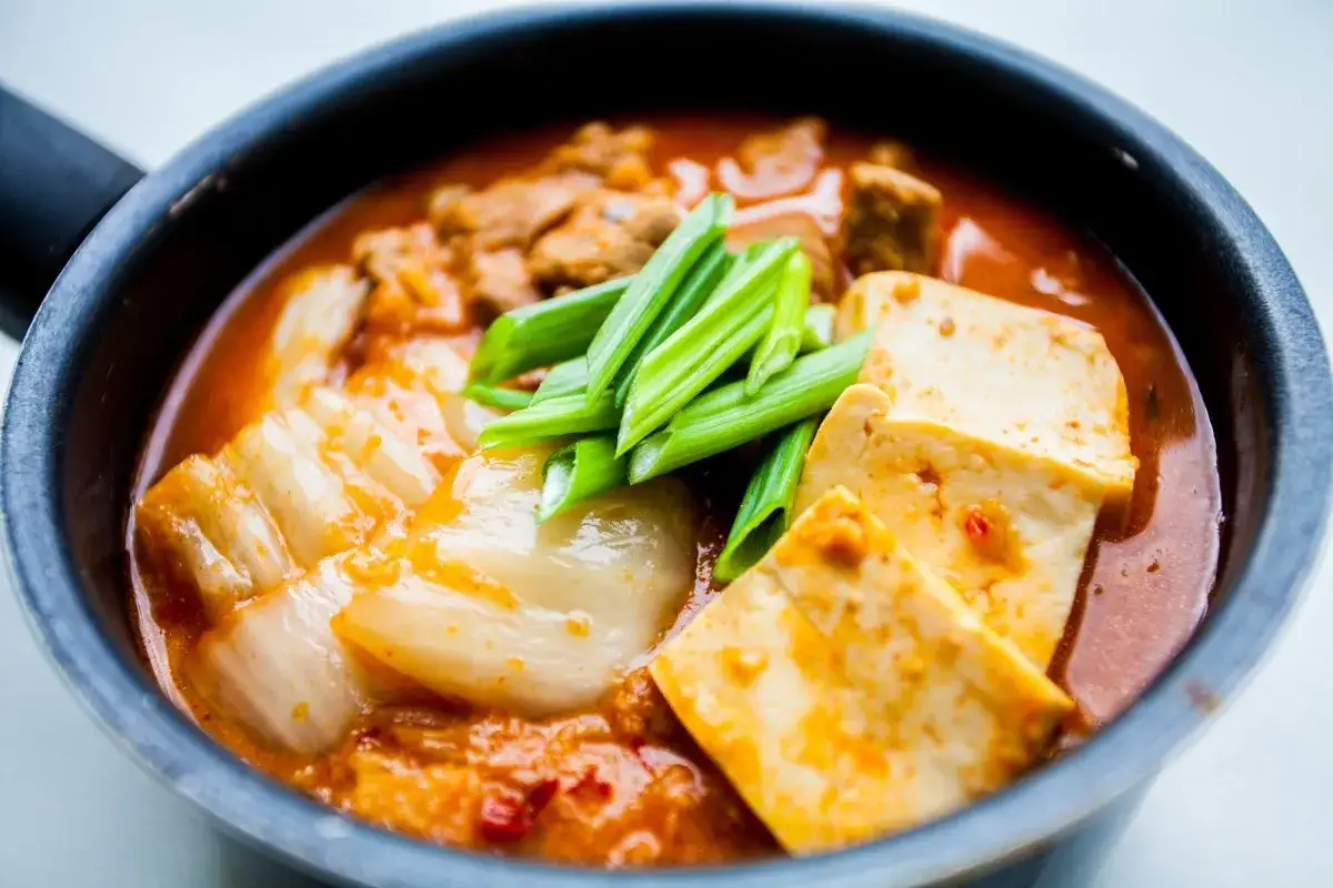 Pyszne koreańskie śniadanie: pikantny bulion z tofu, kapustą kimchi i mięsem, ozdobione szczypiorkiem.