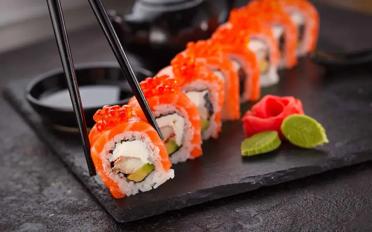 Chopsticks podnoszą rolkę sushi z łososiem i ikrą. Czy sushi jest ciężkostrawne? Zależy od składnik&oacute;w, ale ta wygląda apetycznie!