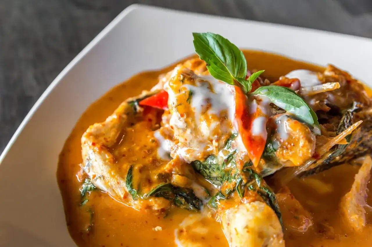 Aromatyczne curry z dorszem w kremowym sosie, ozdobione listkami bazylii i papryczką chili.